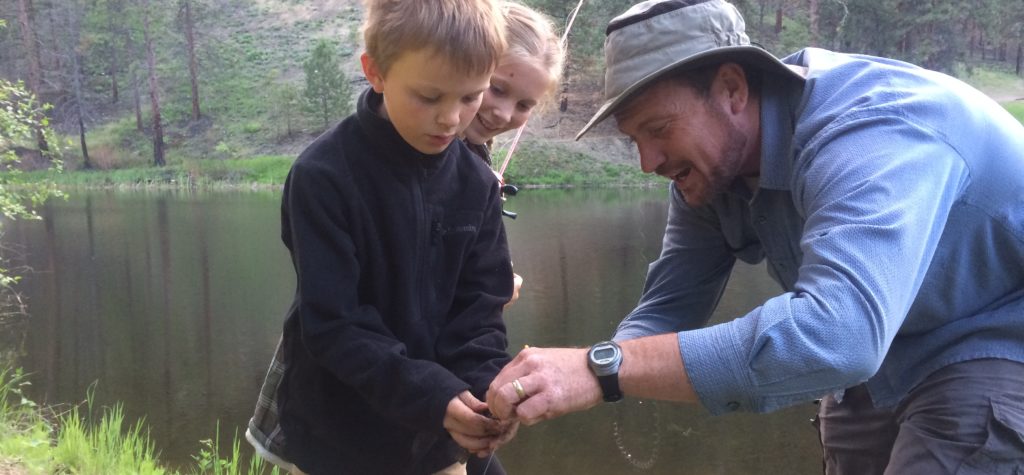 Father helping his children with a fishing hook and line at the river.