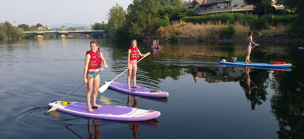 Two teenage girls standing on paddleboards smiling for the camera.