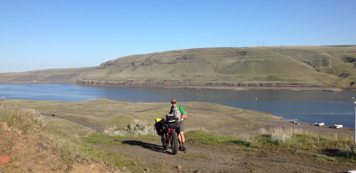 Man standing alongside his bike on the Columbia Plateau Trail State Park aside the Snake River in southeast Washington.