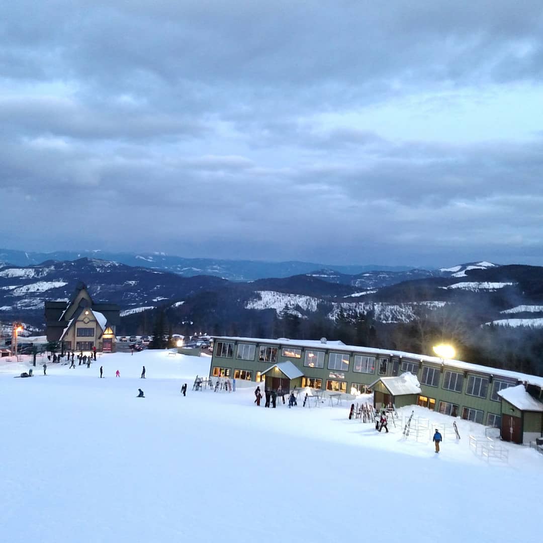View of Mt Spokane ski area at dusk during night skiing with the lodge lights illuminating the snow.