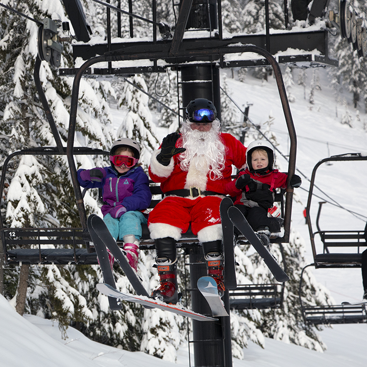 Two young skiers sitting with Santa while riding a chairlift at Lookout Pass.