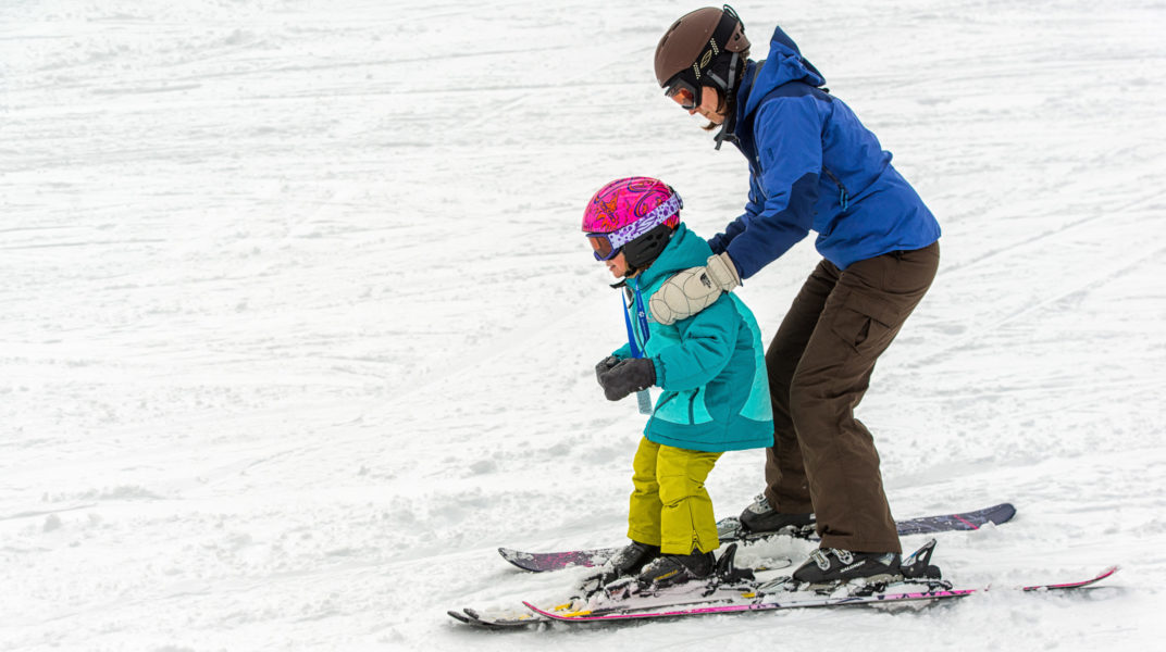 Adult assisting a child, teaching how to ski.