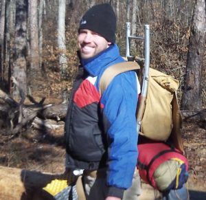 A man smiling with his hiking and camping equipment.