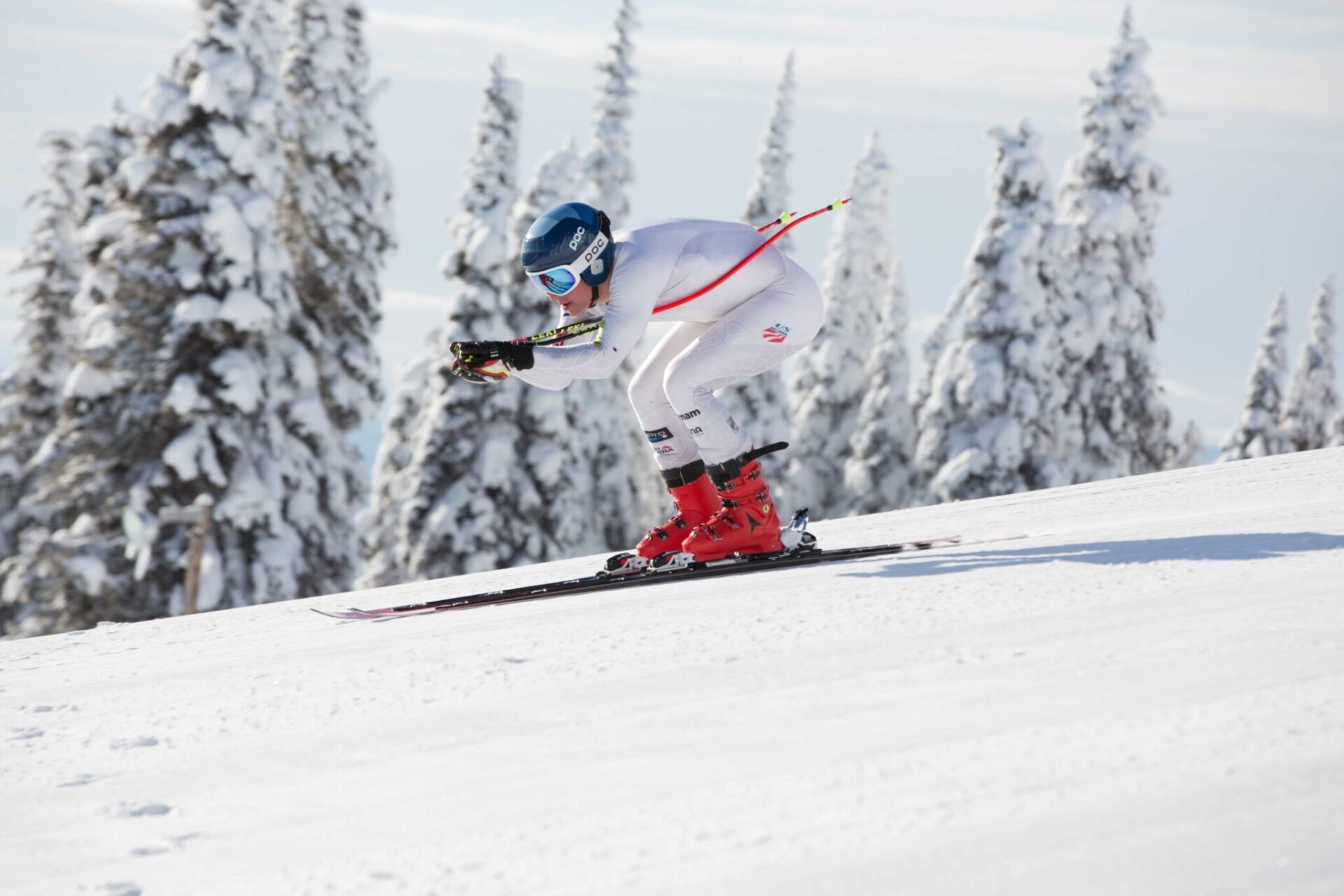 A person ski-racing with white gear and red boots.