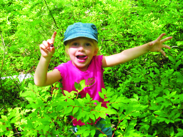 A kid smiling while collecting wild berries.