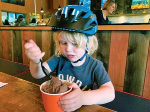 A little kid with a helmet eating icecream.