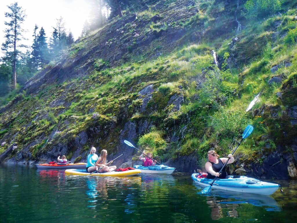 A family of kayakers on Lake Sullivan, along the moss-covered rocky shoreline with a small waterfall.