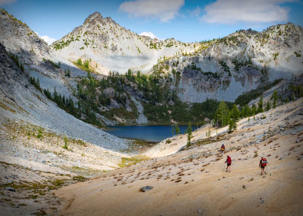 Three people hiking towards a lake.