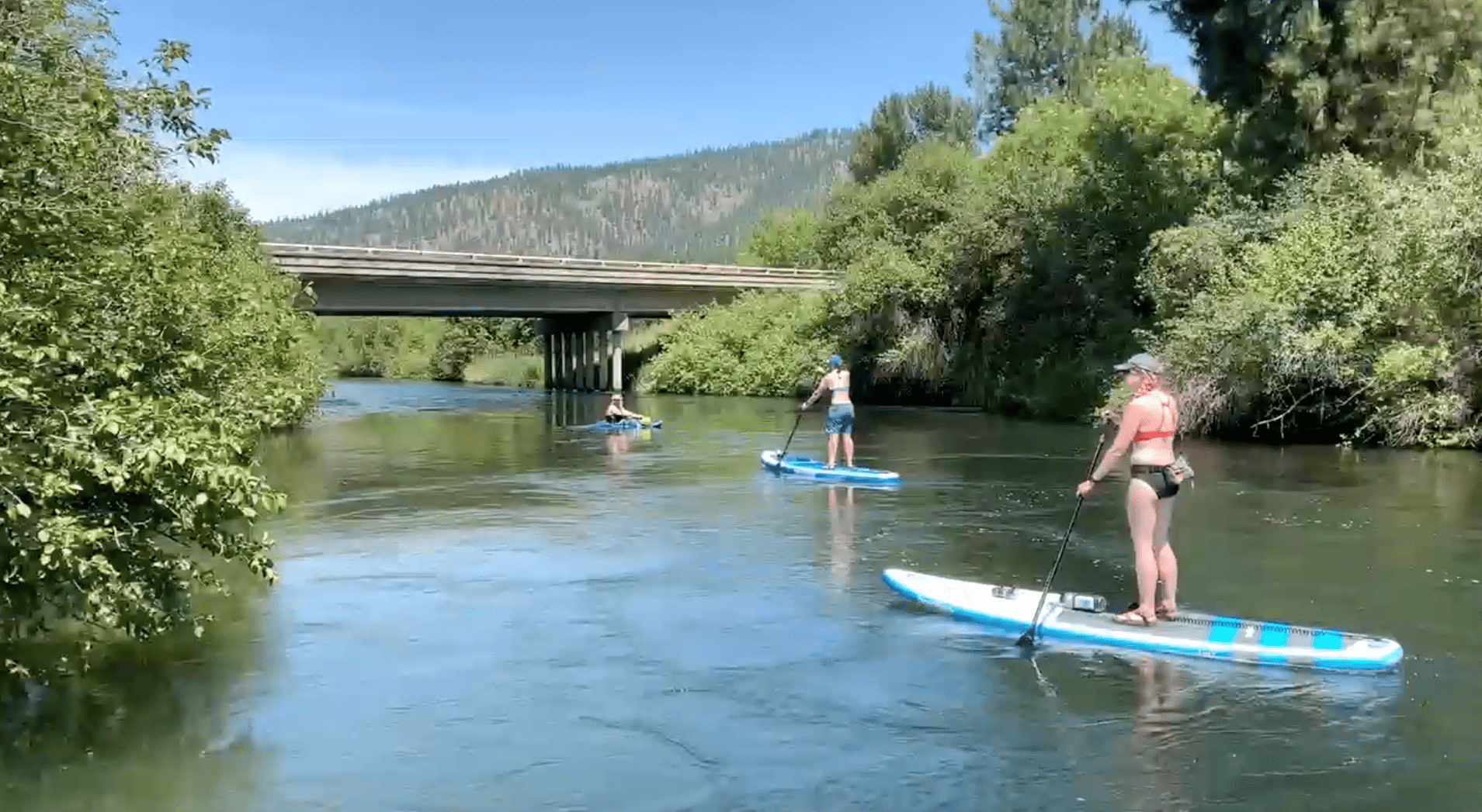 Two people paddle-boarding and one kayaking down a river.