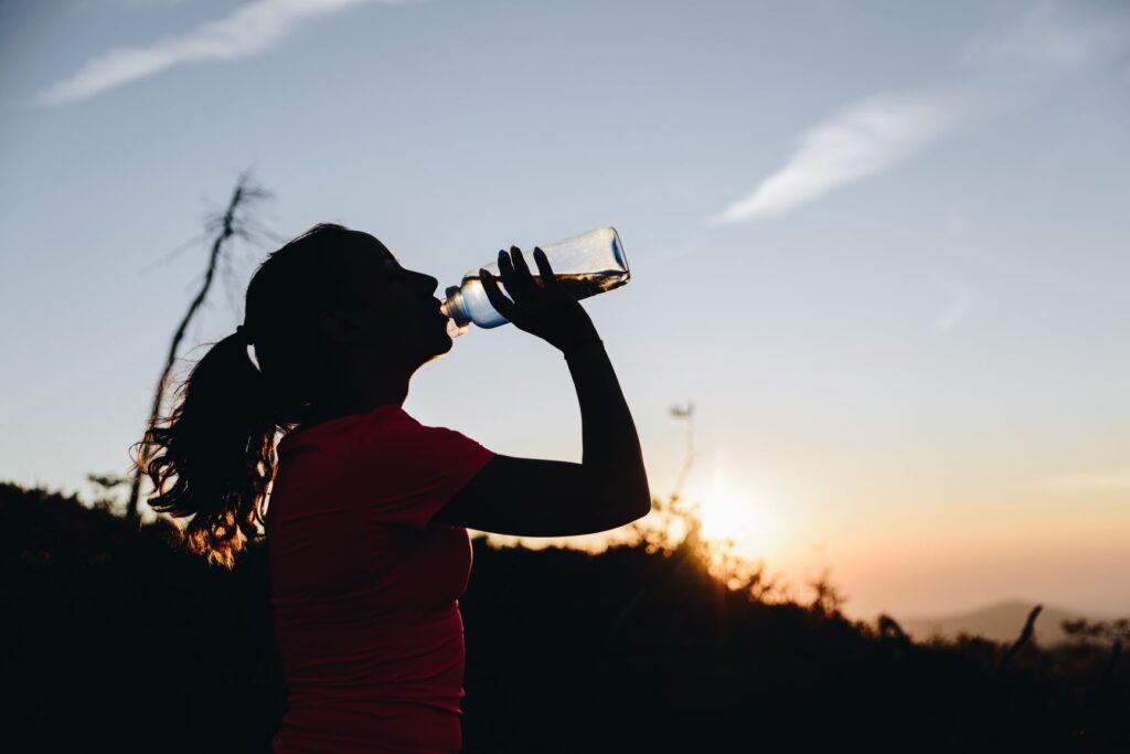woman runner drinking water with sunset in background