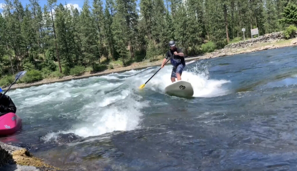 Person paddle-boarding down rapids.
