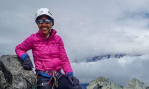 Woman with a pink jacket smiling at the top of a mountain.