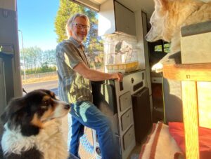 A man smiling at his two dogs and parrot.