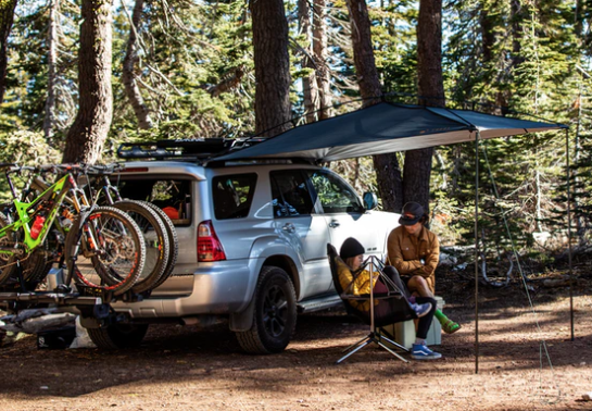 Two people sitting under a portable car awning.