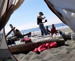 View looking out a tent to the sandy beach, blue sky, ocean horizon, and friends.