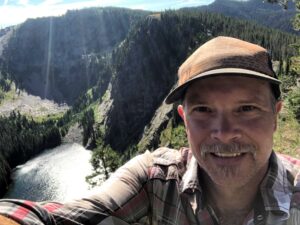 Person taking a selfie on a cliff with a lake at the bottom.