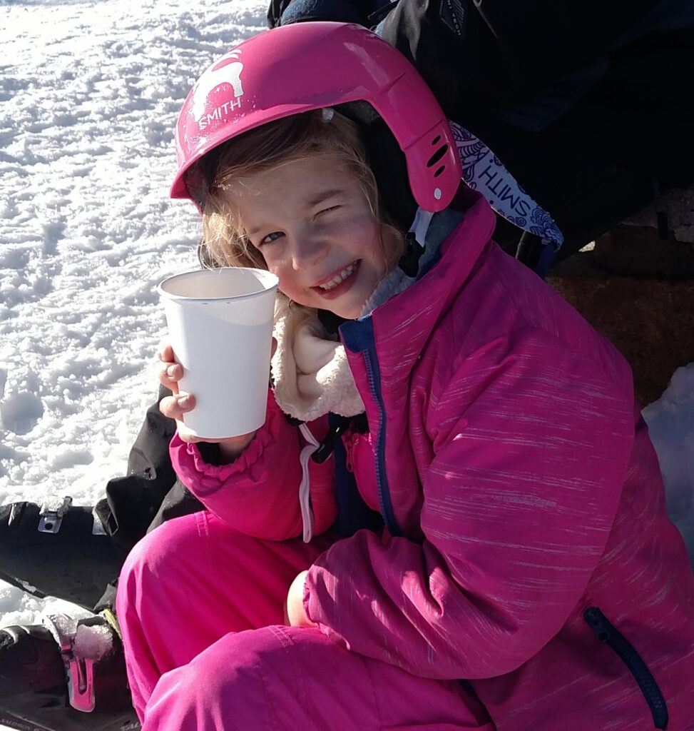 Girl winking while drinking hot cocoa outside in the snow.