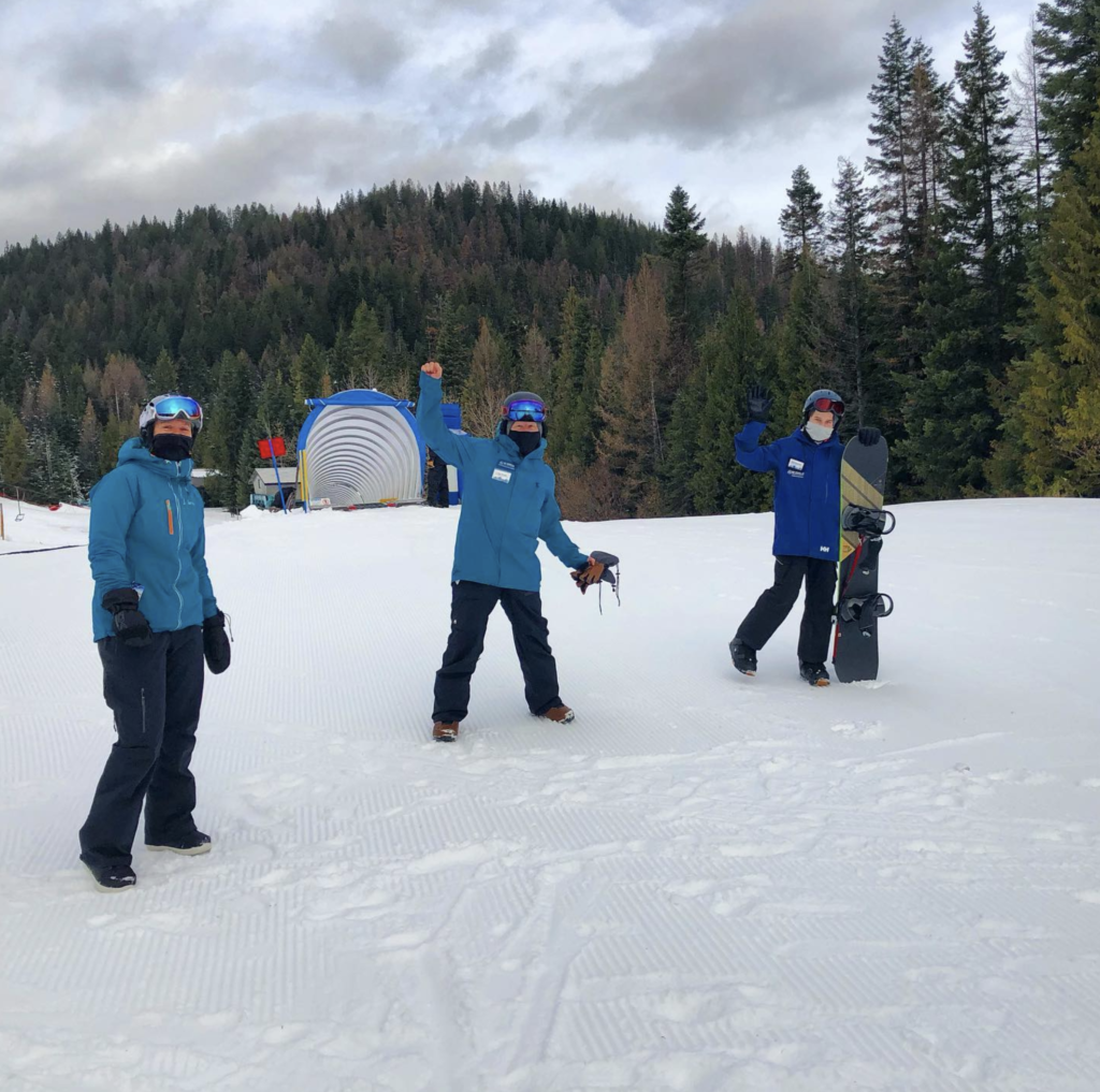 Three employees at 49 Degrees North standing on the snow greeting guests.