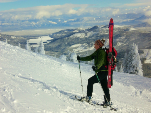 Man snowshoeing up a snowy slope, wearing backpack with skis strapped to it.