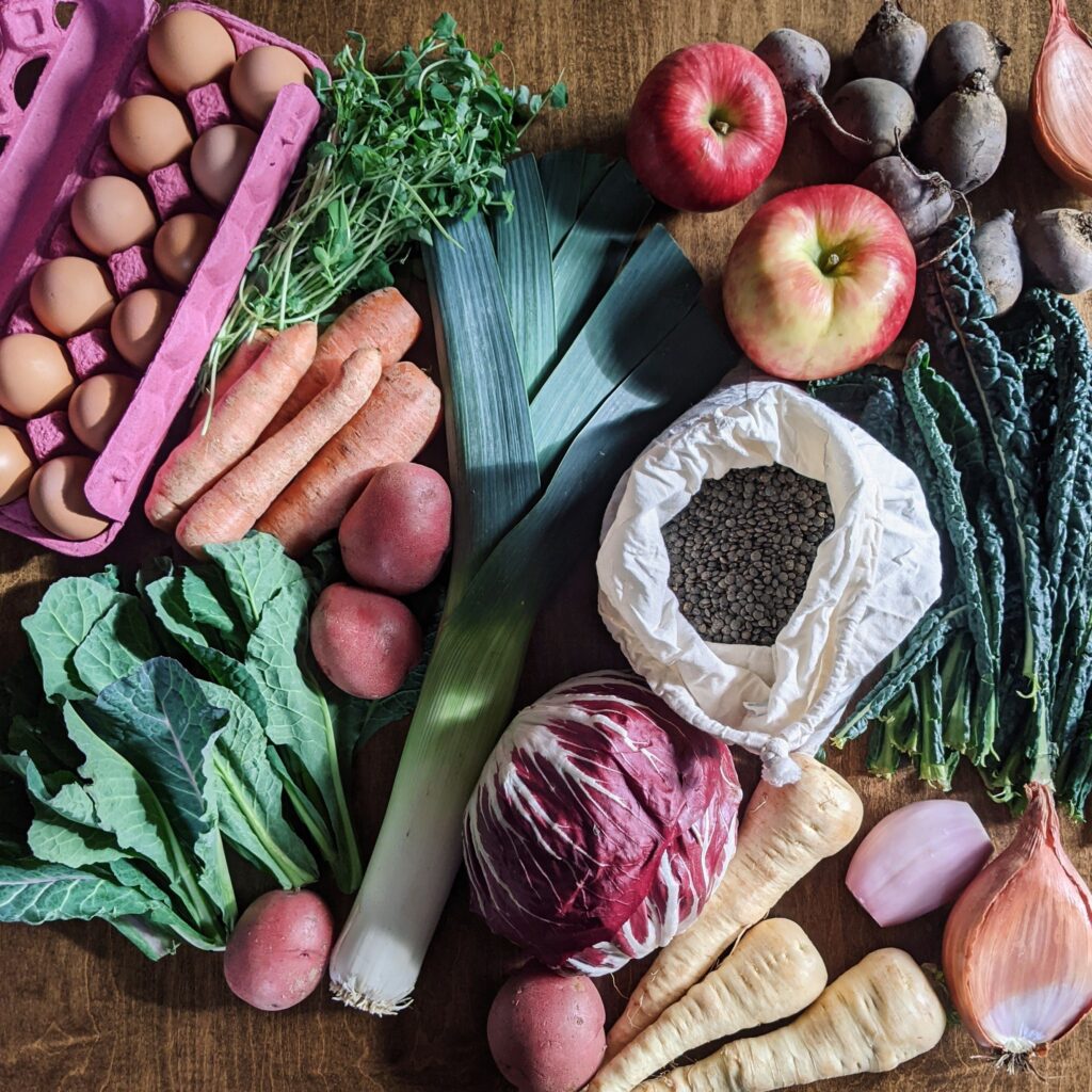 An array of fresh, local food from LINC Foods, including eggs and vegetables, like cabbage, carrots, potatoes, spinach, and turnips.