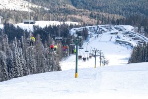 Skiers and snowboarders ride the chairlift to the summit of Mt Spokane, with lodge 2 at the mountain ski area base in the distance.