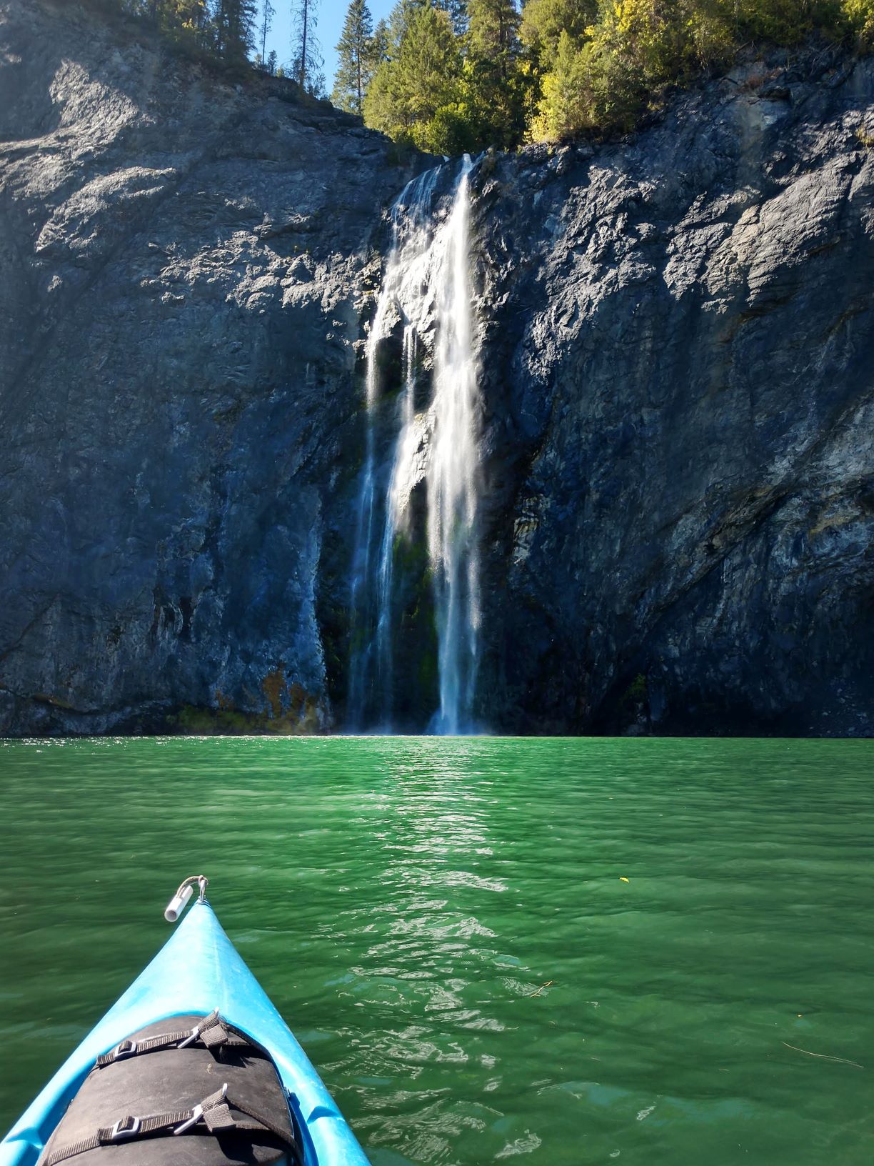 View from a kayak of waterfall, Peewee Falls, over basalt rock into the Pend Oreille River.
