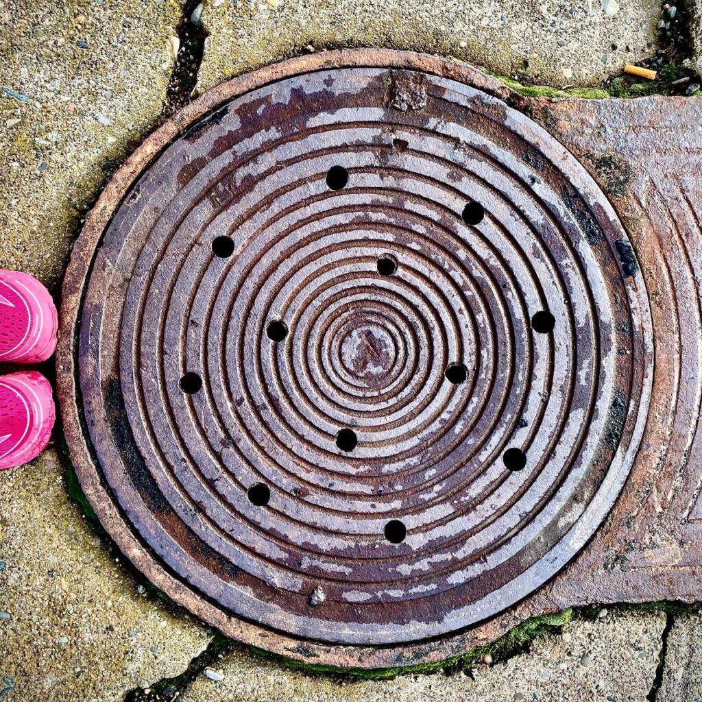 Boots next to a manhole cover on the road.