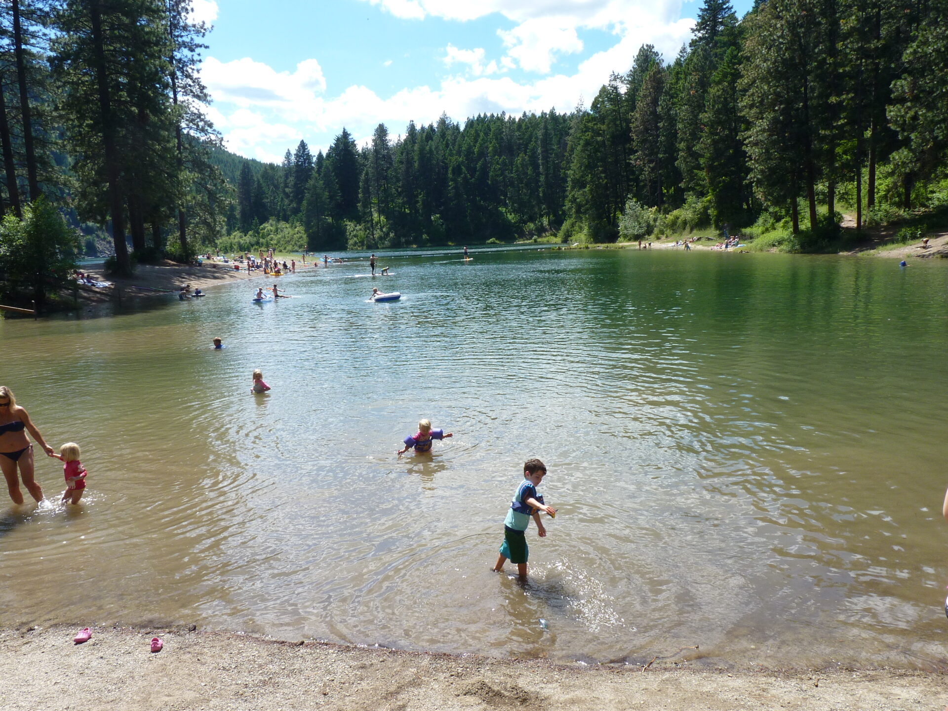 Swimming beach at Farragut State Park, with children and adults swimming, floating on tubes, and paddling.