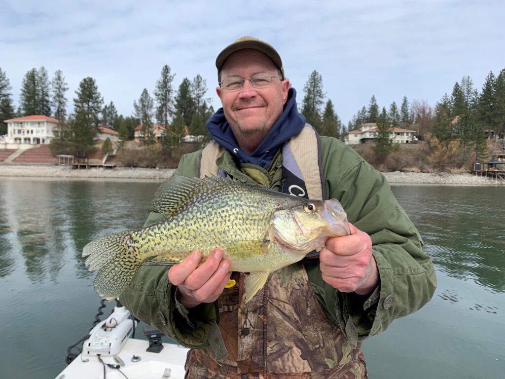 Man holding Black Crappie fish and smiling at the camera.