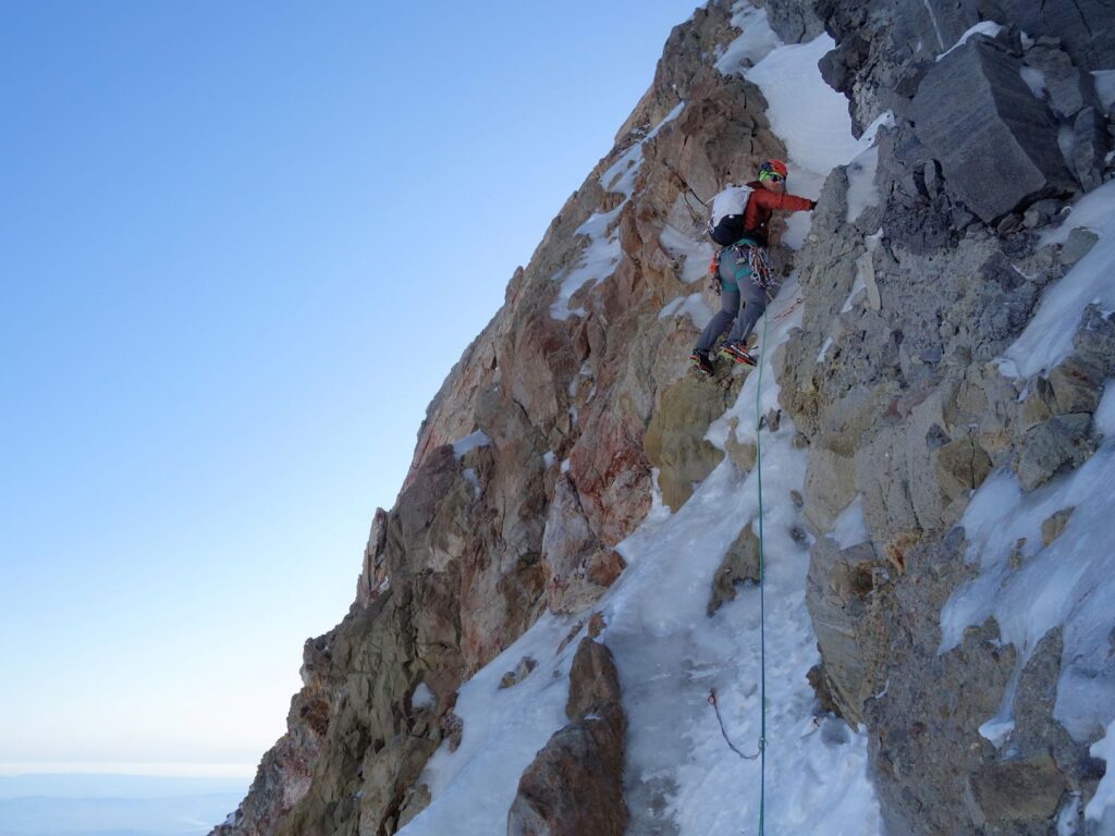 Rock climber Kyle Tarry ascending a vertical rock slope on Mount Hood, ice climbing on a ribbon of ice.