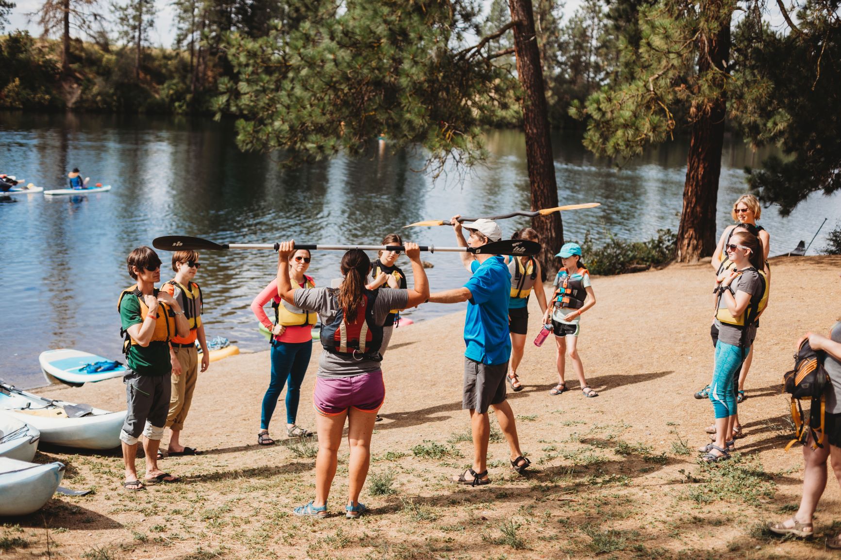 People standing on a sandy beach getting instructions on how to properly hold and use a kayak paddle during the Spokatopia Outdoor Adventures Festival in Spokane, WA.