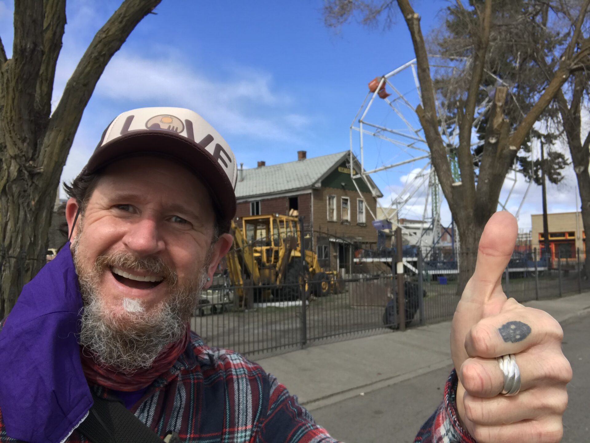 Man taking a selfie with thumbs-up sign to celebrate his walk in a new neighborhood in Spokane. House and street in background.