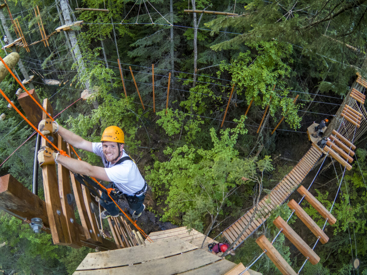 Man holding on to a wooden aerial ladder among trees at Mica Moon.