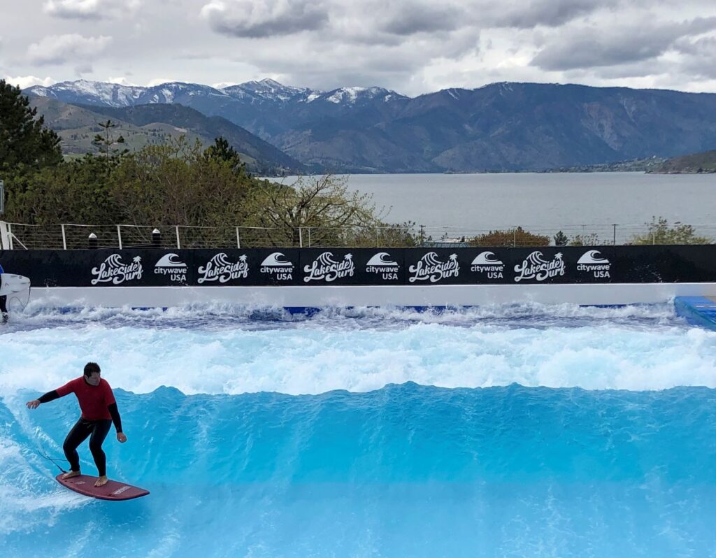 Man surfing the standing, stationary wave at Lakeside Surf, with view of Lake Chelan in the background.