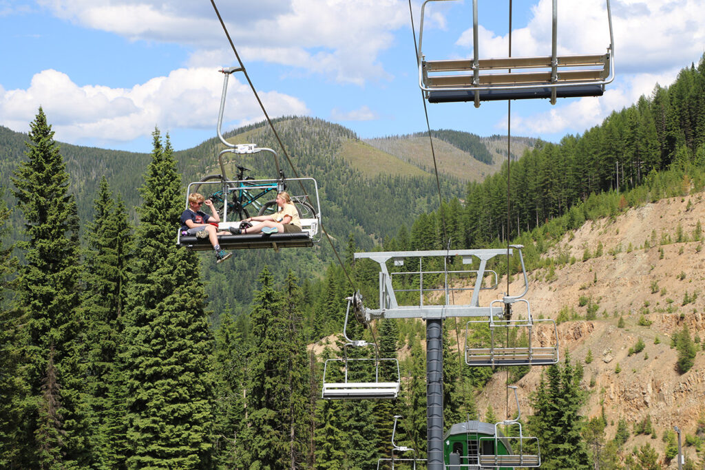 People riding a chairlift at Lookout Pass during summer to access hiking and mountain biking trails.