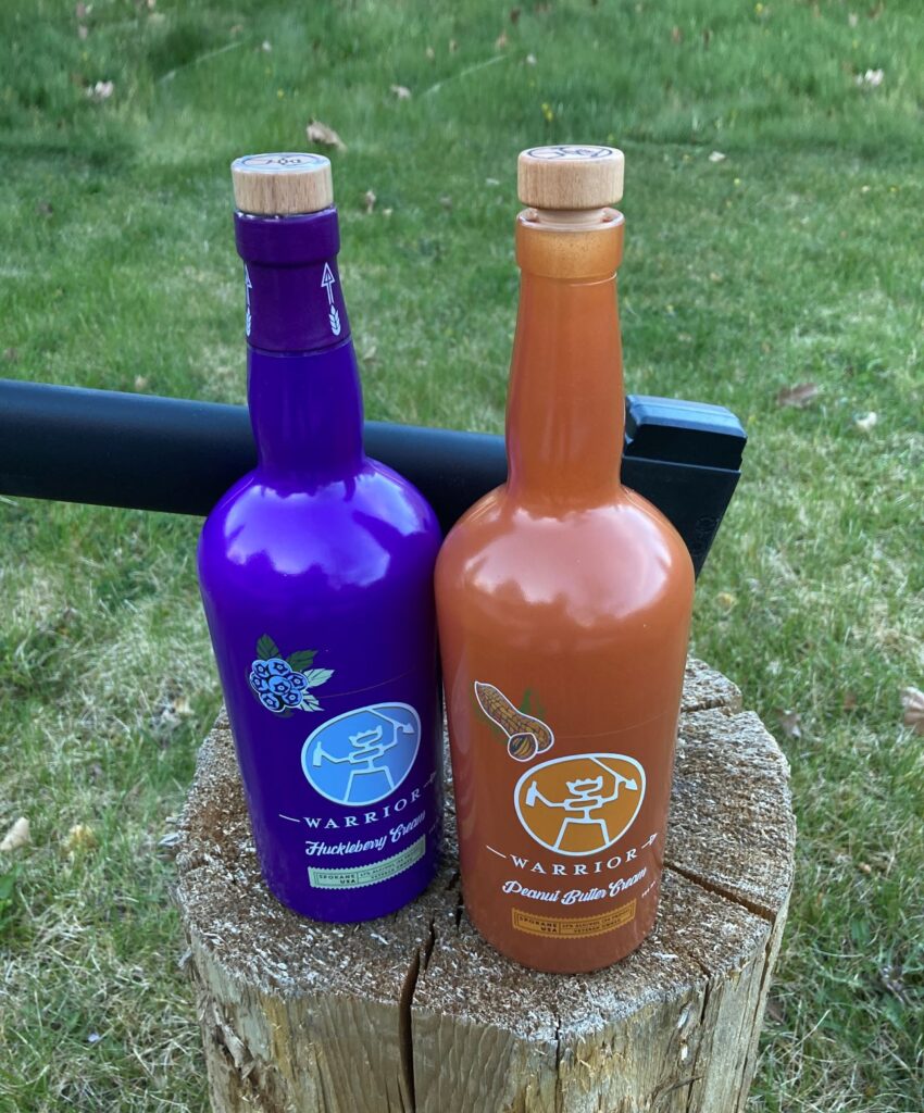 Two colored bottles of Warrior Liquor, including Huckleberry and Peanut Butter Cream.