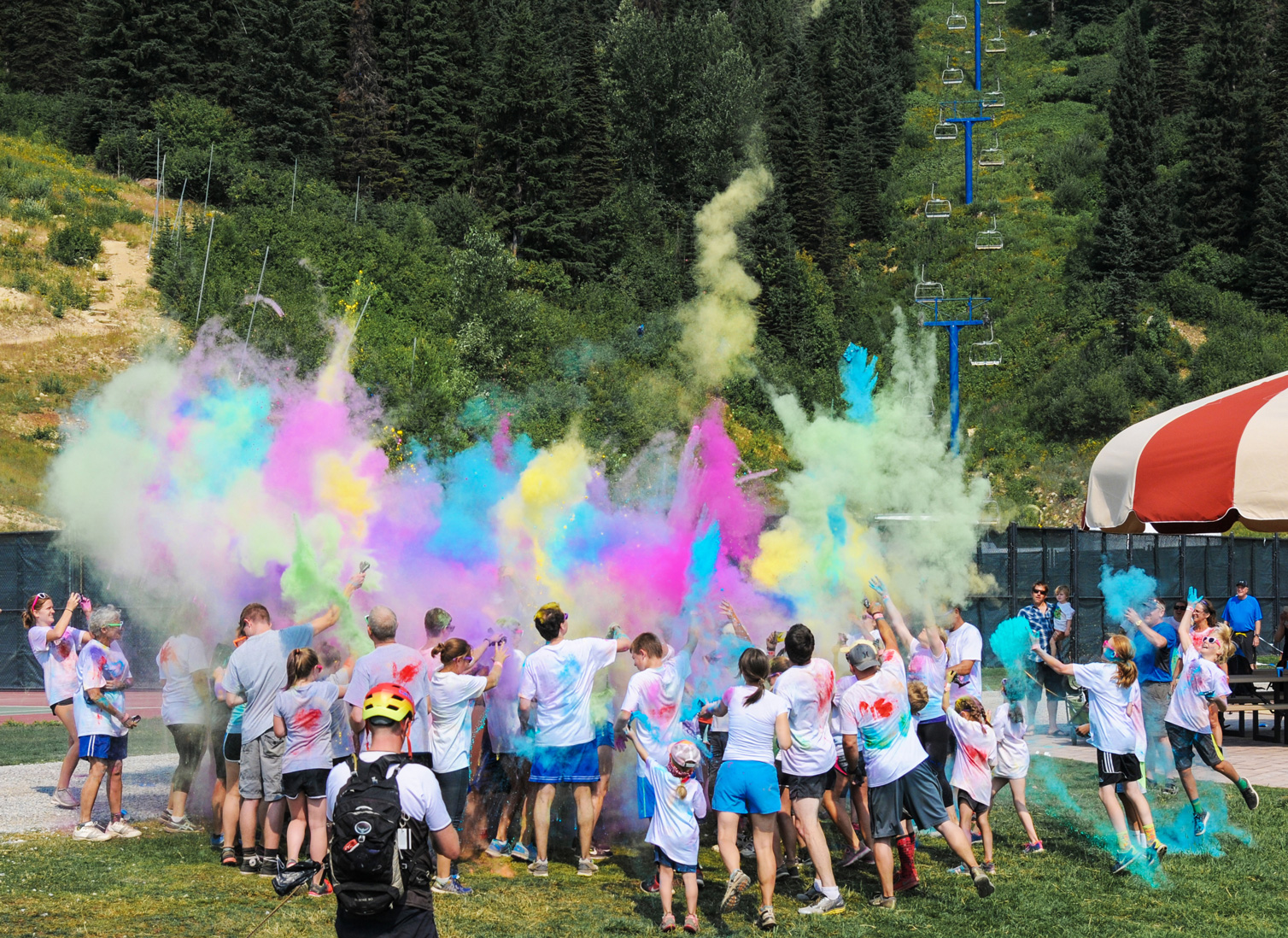 Parents and children enjoying the Huckleberry Color Fun Run at Schweitzer, with colored chalk in the air.