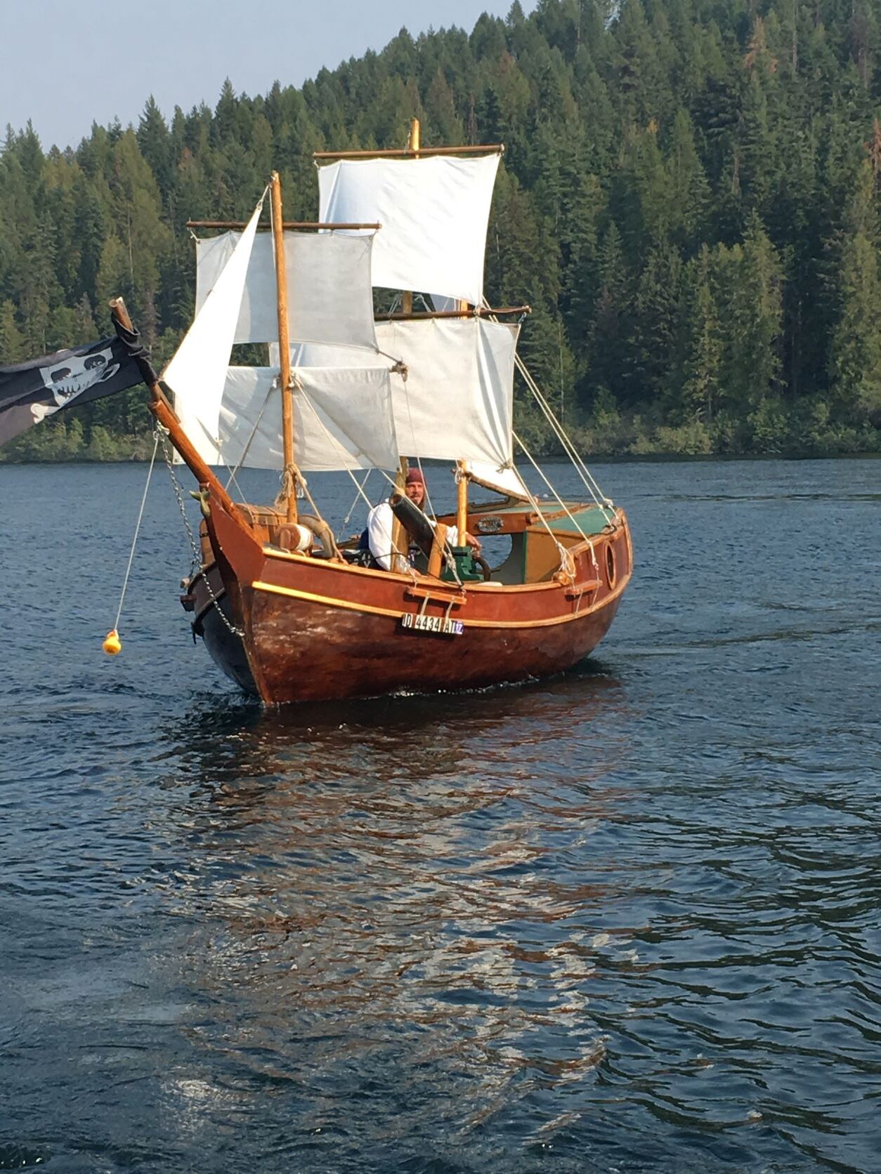 Pirate boat on Lake Pend Oreille, with white sails and wooden hull, with Captain Dan steering.