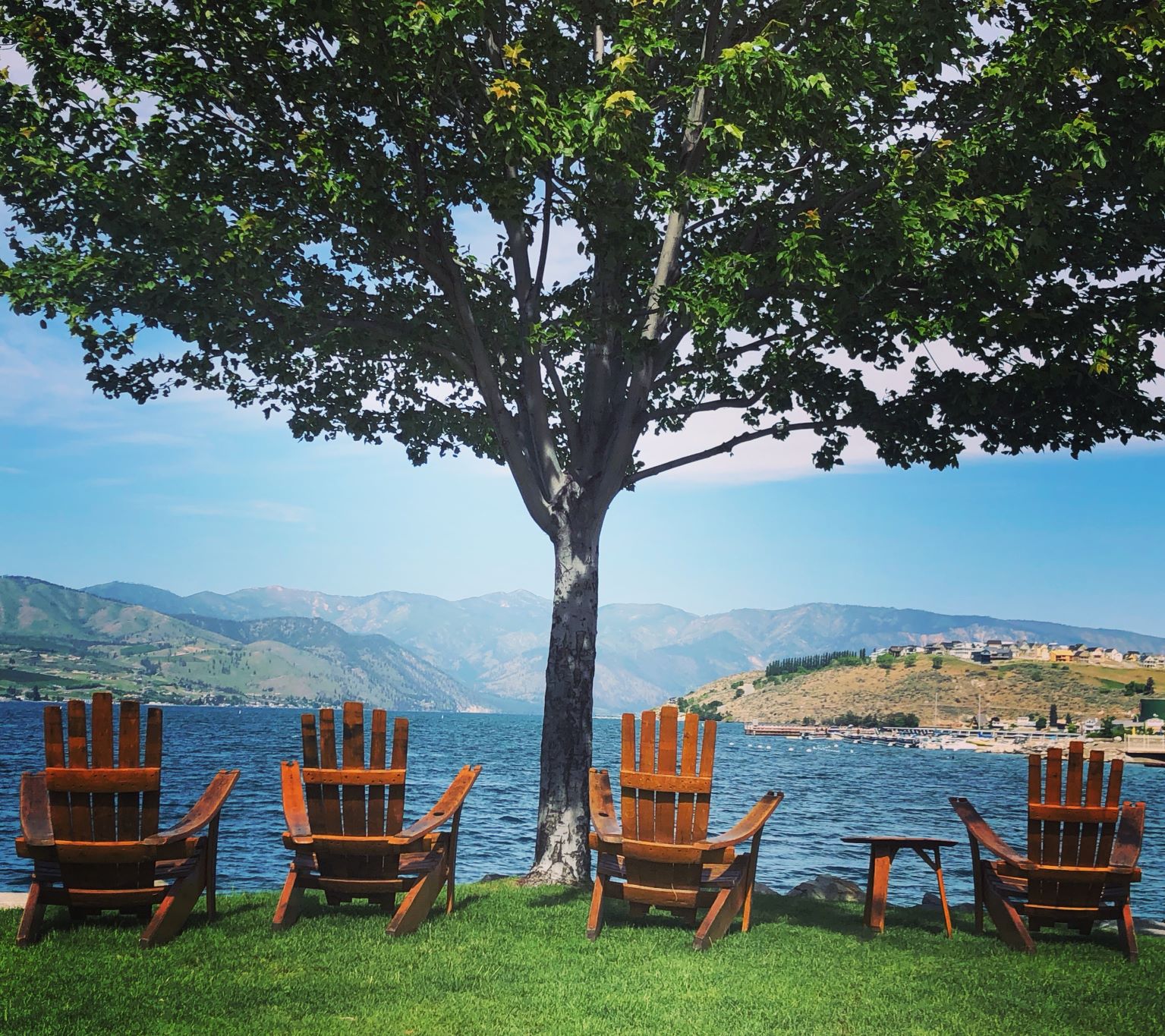 Four Adirondack chairs facing out towards the blue water of Lake Chelan.