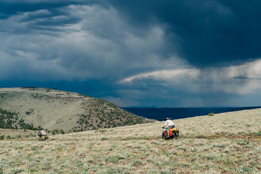 Biking down the east slope of Steens Mountain in Oregon, with dark storm clouds looming in the distance.