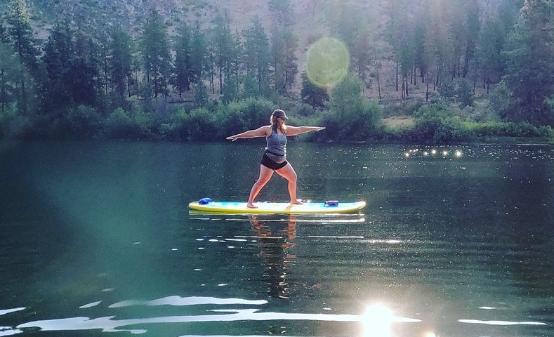Woman doing a yoga pose while on a stand-up paddleboard on a lake.