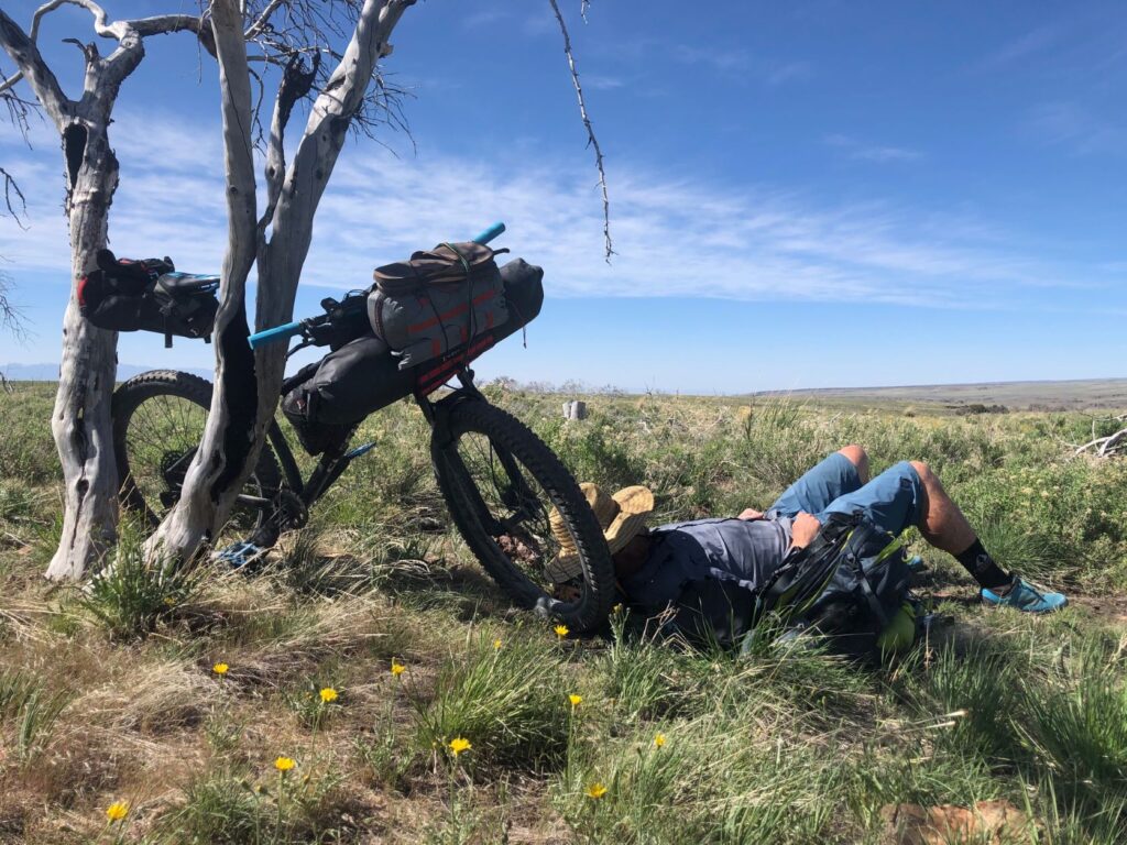 Man napping in the shade, leaning against his bike, in the remote landscape of southeast Oregon.