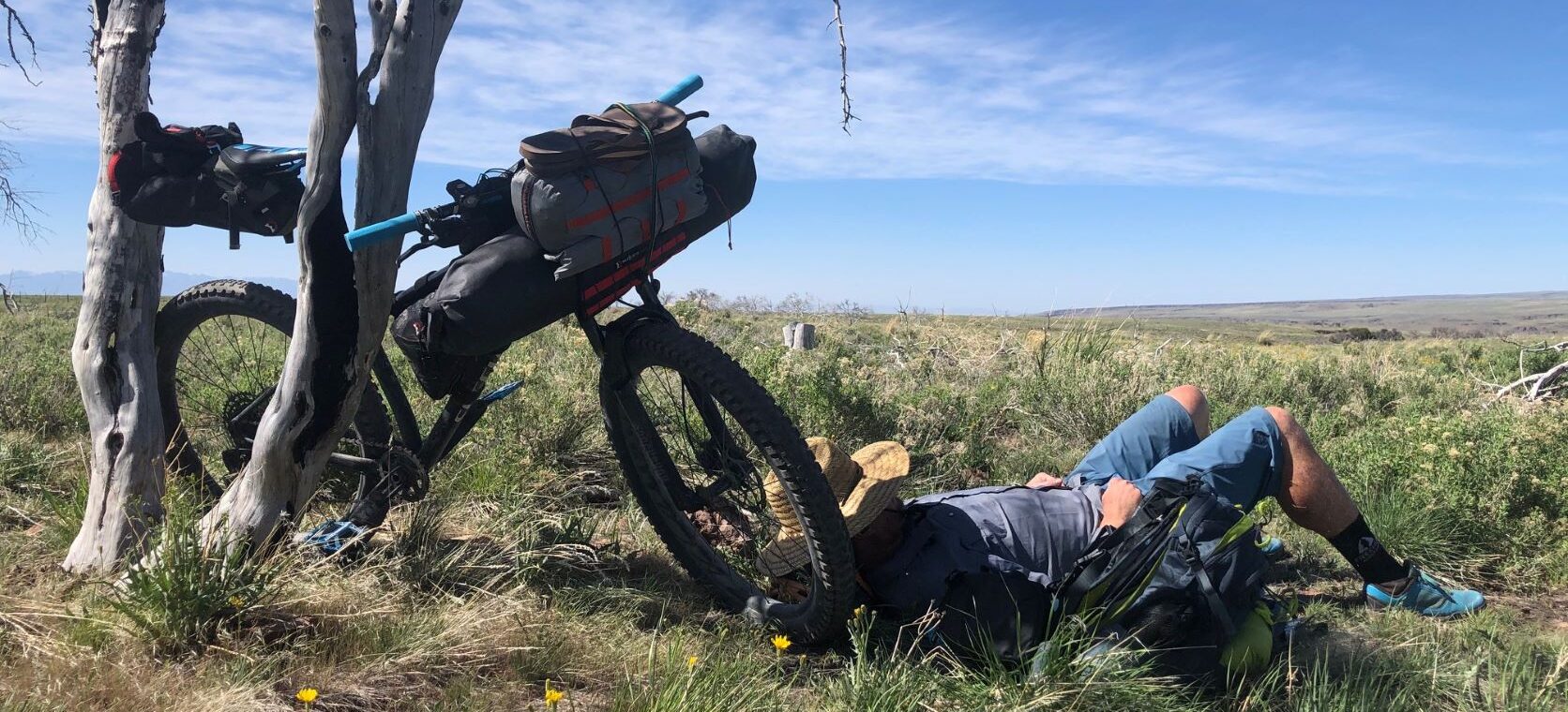 Man napping in the shade, leaning against his bike, in the remote landscape of southeast Oregon.