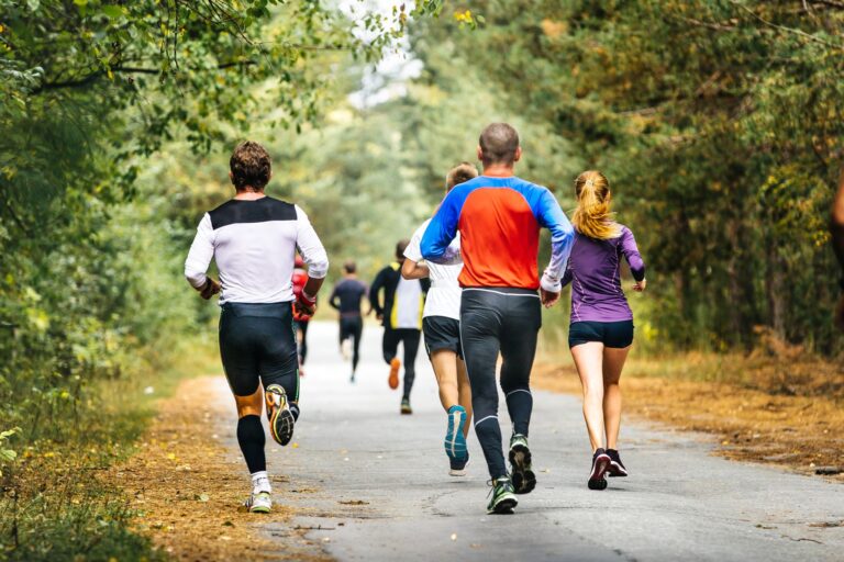 Group of runners on a paved trail in a treed park.