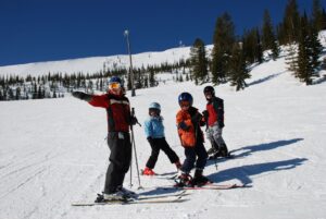 Ski instructor pointing downhill while teaching a group of three young skiers at Schweitzer Mountain.