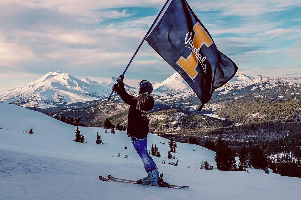 Ski team member on the mountain waving a U of I Vandals flag.