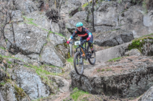 A mountain biker riding on a singletrack trail and over boulders on Beacon Hill.