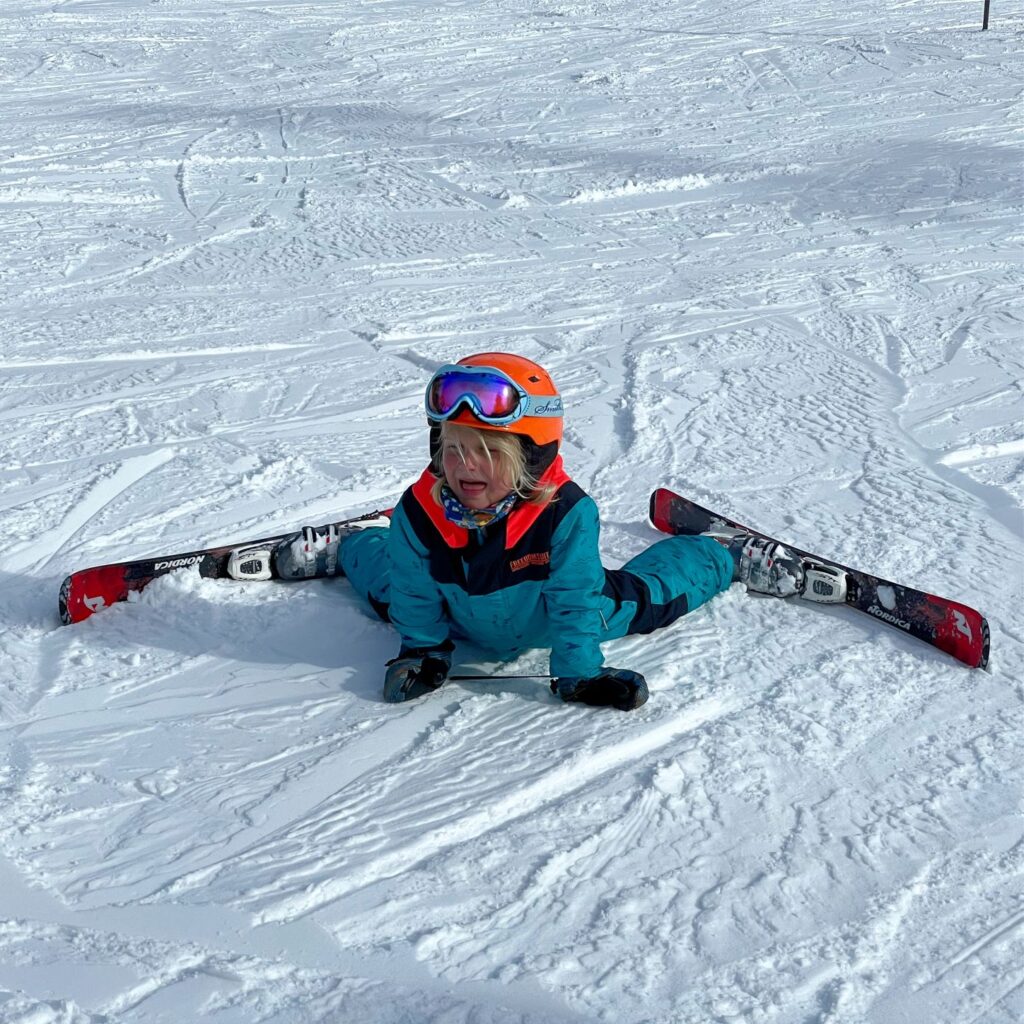 Remi doing the splits while wearing skis on the bunny hill.