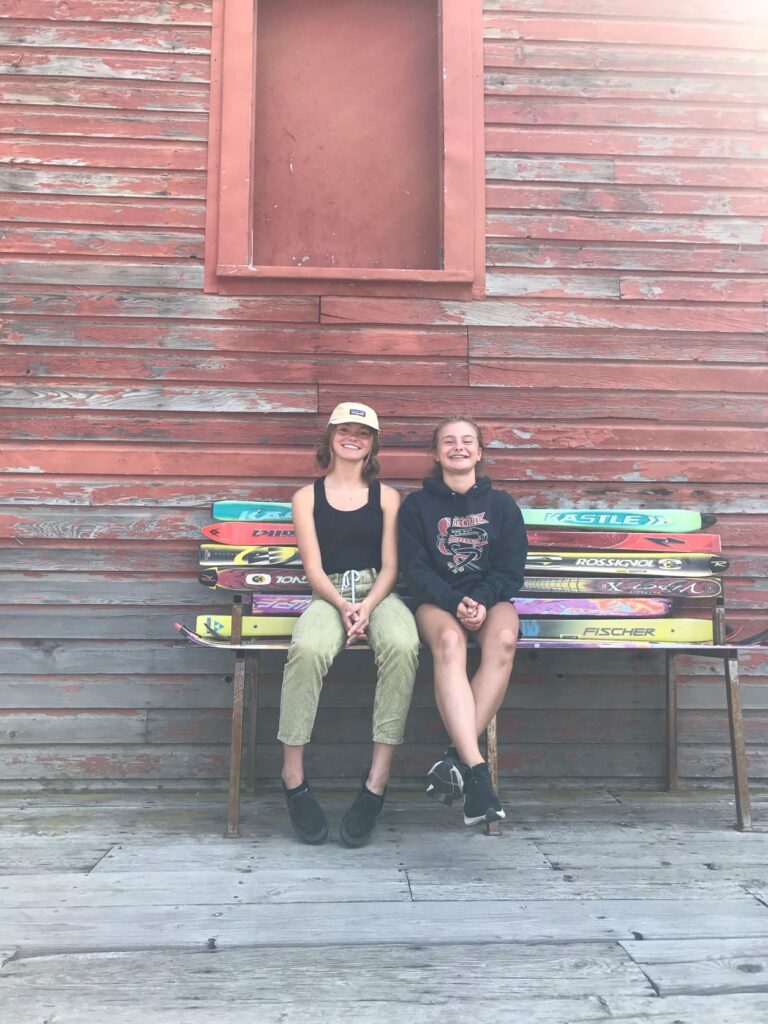 Sisters Emma and Maddie Hall sitting on a bench crafted from old alpine skis.