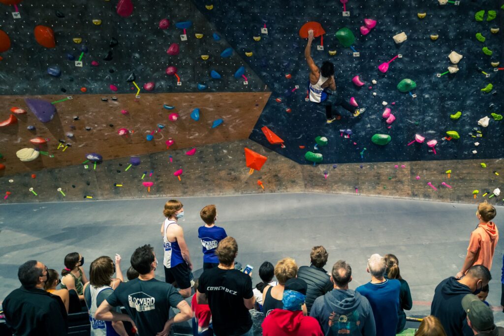 Ethan Anderson on the bouldering climbing wall during competition while spectators look on.